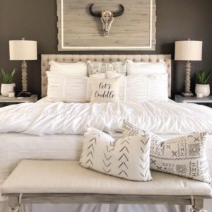 Farmhouse tuft bed with white bedding and a faux bull skull hanging on wall.