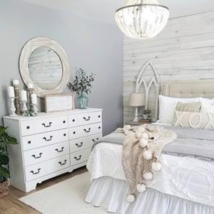 Gray and white farmhouse master bedroom with white dresser and rustic candlesticks. A gorgeous beaded chandelier and tuft headboard.