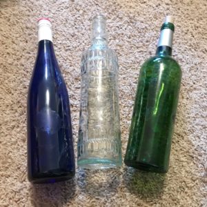 a blue wine bottle, green wine bottle, and a clear vintage bottle.